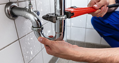 a man fixing a leaking sink pipe using a wrench