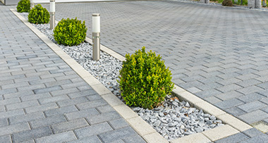 a newly laid double driveway of a home with small bushes and lights separating the two driveways