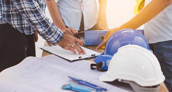 a group of people standing together overlooking building plans with hard hats sat next to them