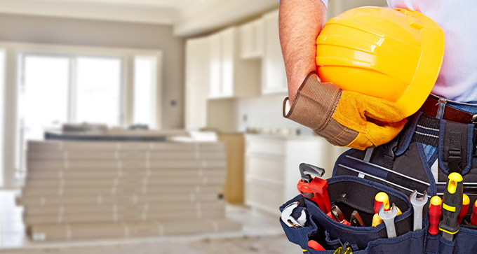 a builder holding their hard hat with a belt of tools, standing in a residential home under refurbishment