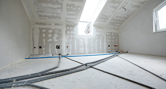 a room in a home under a refurbishment, with bare walls and exposed floor with pipes