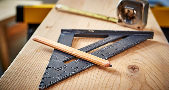 a set square, pencil and tape measure on top of a slab on hardwood