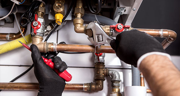 a heating technician tightening the bolt on a gas boiler system