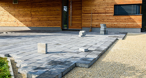 a grey brick driveway being laid outside of a wooden property